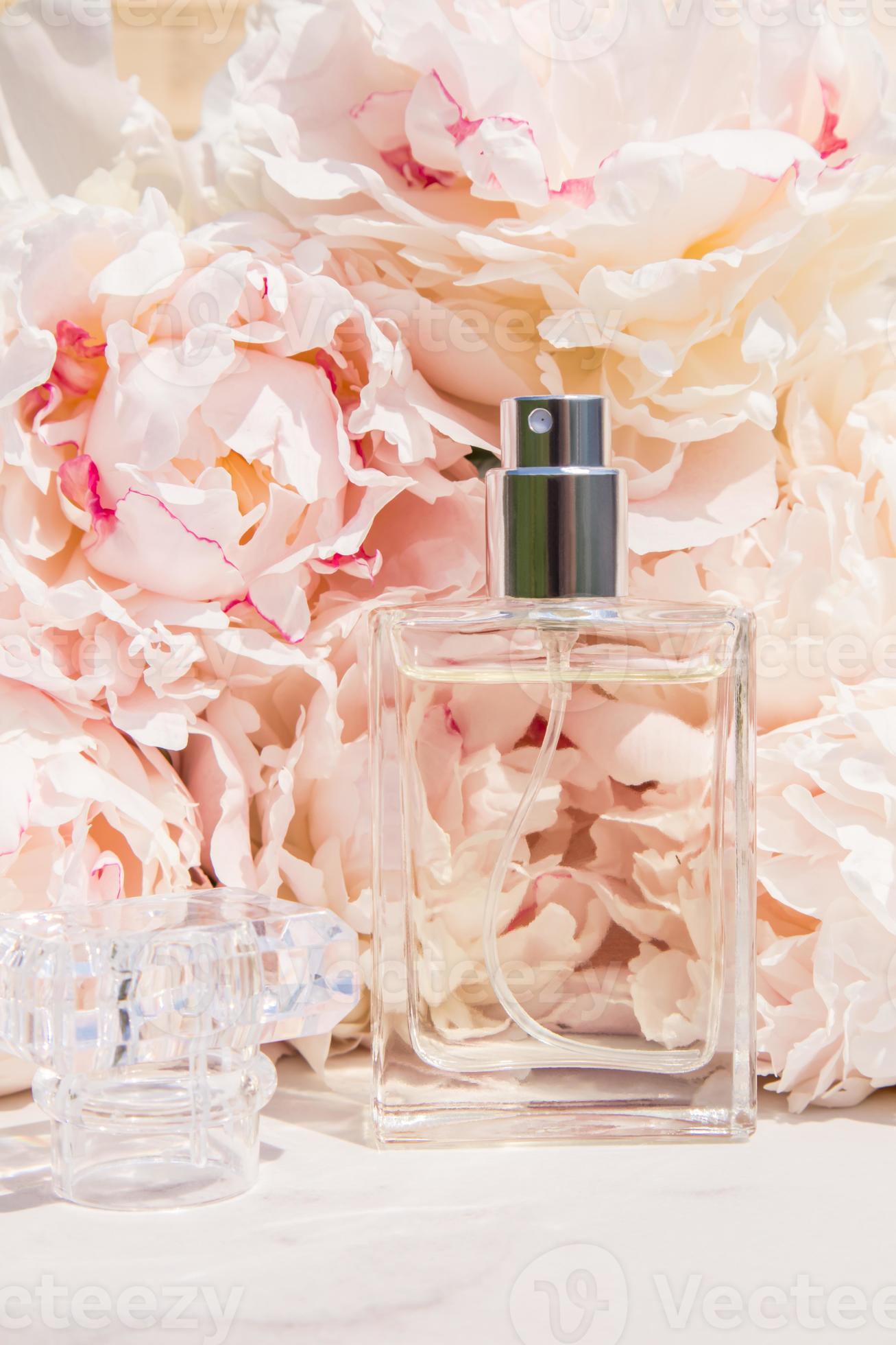 a bottle of perfume made of transparent glass against the background of pink peonies presentation of fragrances advertising of a cosmetic product photo